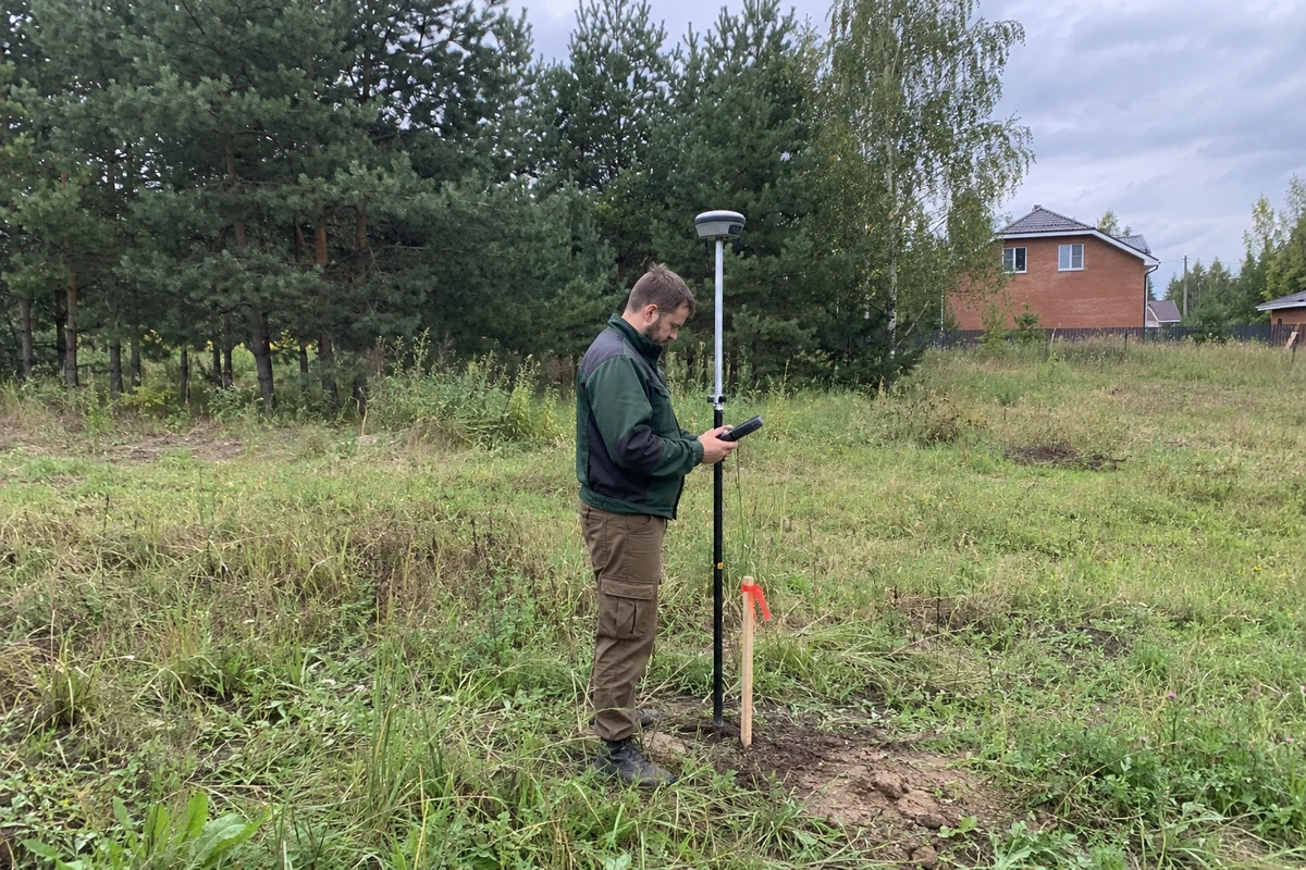 Геодезист с GNSS-приёмником у закреплённой точки границы участка