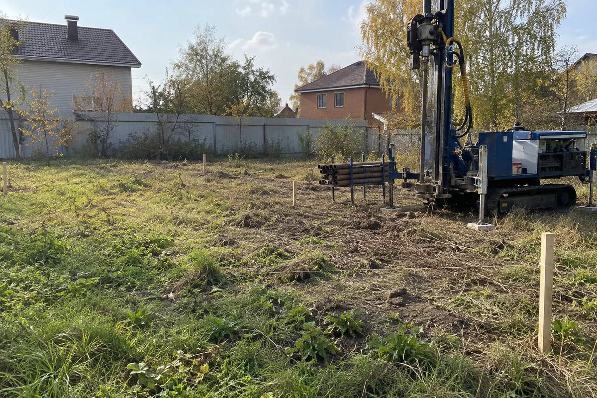 Буровая установка у колышков будущего дома на свободной площадке